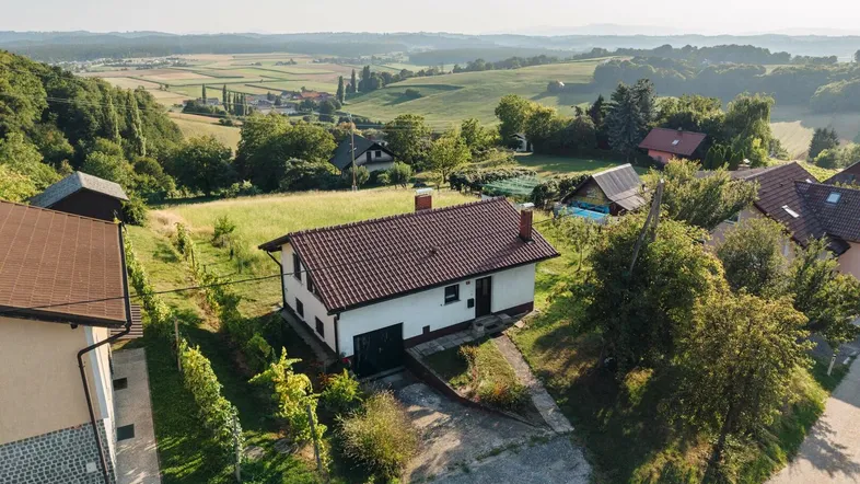 Luftaufnahme eines Hauses mit rotem Dach inmitten einer grünen Hügellandschaft mit Weinbergen.