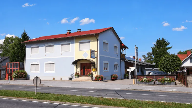 Traditionelles Gebäude mit hellblauer und gelber Fassade, umgeben von Grünflächen und einer Straße.