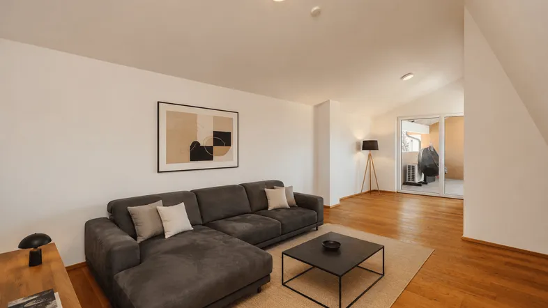 Helles Wohnzimmer mit modernem Sofa, Holzboden und Zugang zu einem Außenbereich.