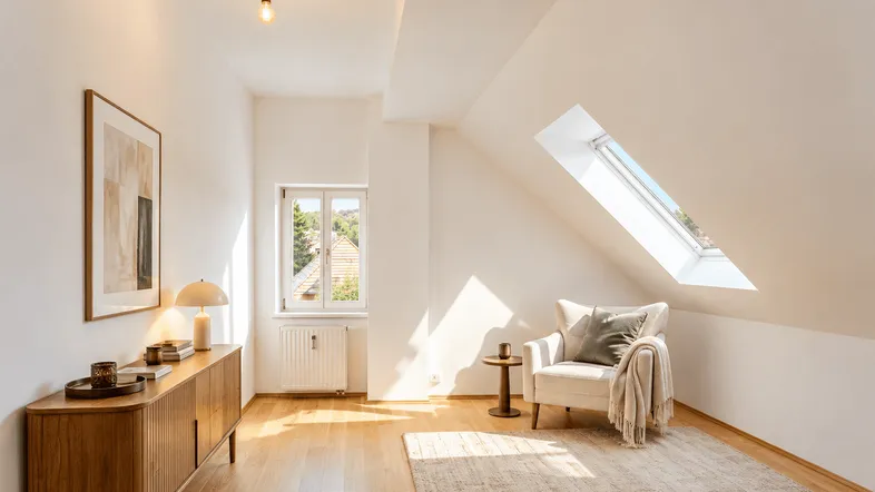 Helles Dachzimmer mit gemütlichem Sessel, Holzboden und Dachfenster, durchflutet von Sonnenlicht.