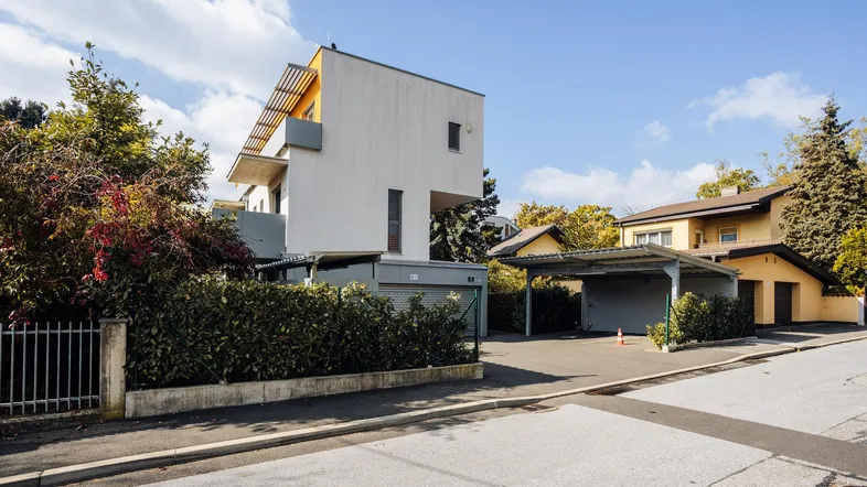 Modernes Wohngebäude mit klarer Architektur, umgeben von Bäumen und einem Carport.