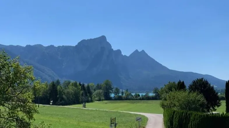 Berglandschaft mit grünen Wiesen und einem See im Hintergrund unter klarem blauem Himmel.