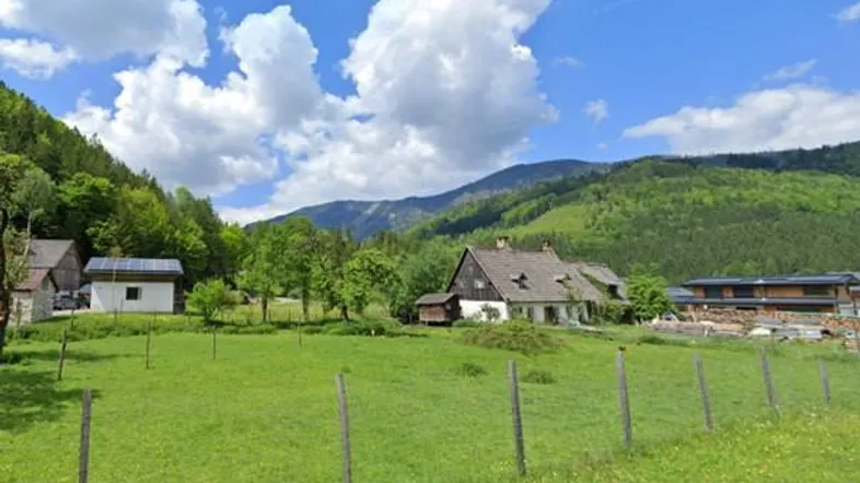 Ländliches Anwesen mit traditionellem Haus, umgeben von grünen Wiesen und bewaldeten Bergen.