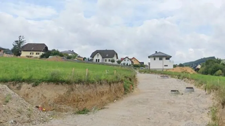 Blick auf eine ländliche Umgebung mit einem unbefestigten Weg und mehreren Häusern im Hintergrund.