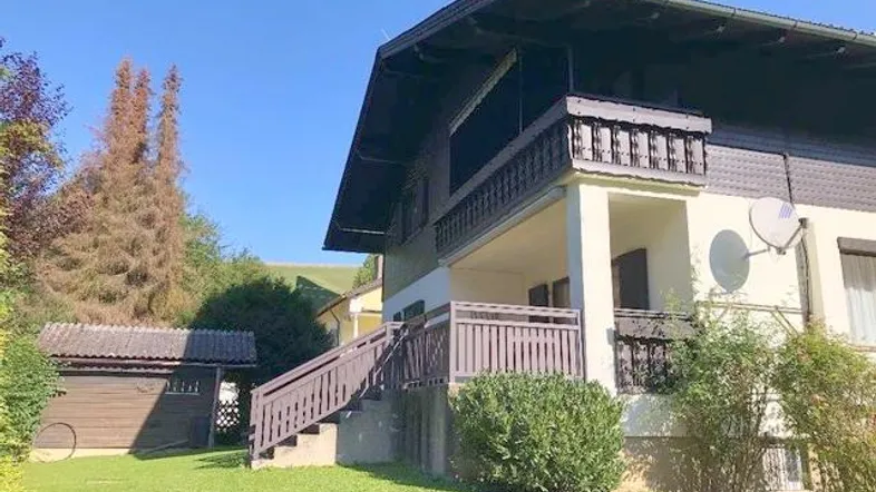 Hausfassade mit Balkon, Außentreppe, Garten und einem kleinen Schuppen im Grünen.