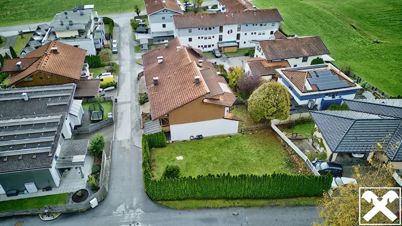 Luftaufnahme eines Wohngebiets mit Einfamilienhäusern, grünen Gärten und einer Straße.