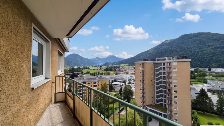 Balkon mit weitem Blick über die Stadt und die umliegende Berglandschaft unter blauem Himmel.