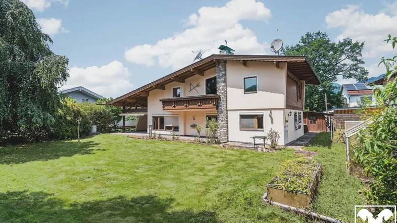 Traditionelles Haus mit großem Garten und gepflegter Rasenfläche unter blauem Himmel.