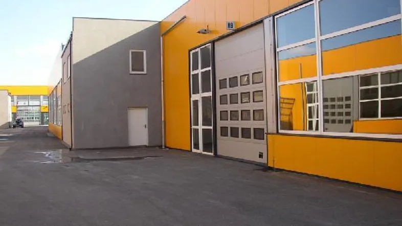 Moderne Gewerbehalle mit gelber Fassade und großen Rolltoren, umgeben von einem asphaltierten Vorplatz.