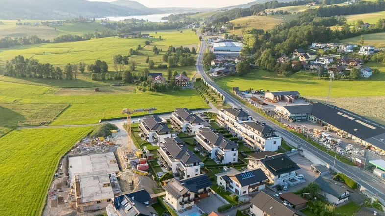 Luftaufnahme einer ländlichen Wohngegend mit Neubauten, einer Straße und einem See am Horizont.