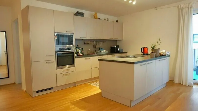 Moderne Küche mit integrierten Geräten, Kücheninsel und Zugang zum Balkon. Helles Eichenparkett.