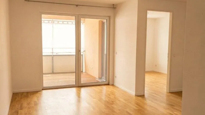 Heller, leerer Raum mit schönem Parkettboden und direktem Zugang zu einem sonnigen Balkon.
