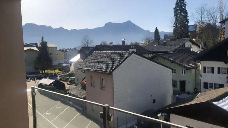 Blick vom Balkon über eine Wohnsiedlung mit Bergen und See im Hintergrund an einem sonnigen Tag.