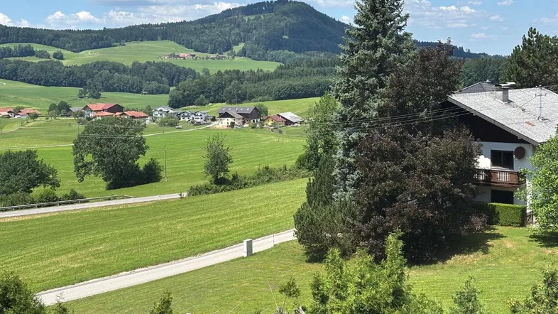 Panoramablick auf die grüne Hügellandschaft mit einem traditionellen Haus und Balkon im Vordergrund.