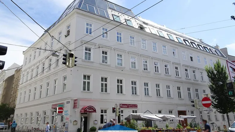 Mehrstöckiges Eckgebäude mit klassischer Fassade, Dachausbau und Geschäften im Erdgeschoss.