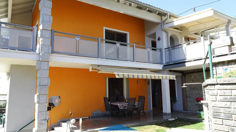 Hausfassade mit orangefarbenem Anstrich, Balkon und einer möblierten Terrasse im Erdgeschoss.