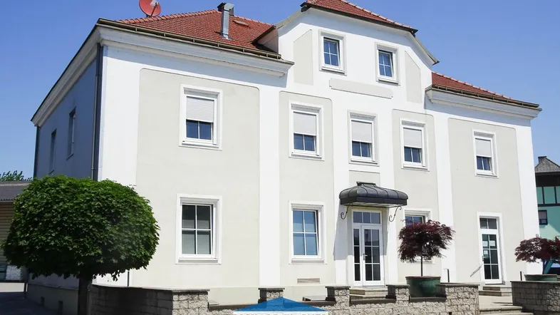 Klassisches Mehrfamilienhaus mit weißer Fassade, roten Ziegeln und gepflegtem Eingangsbereich.