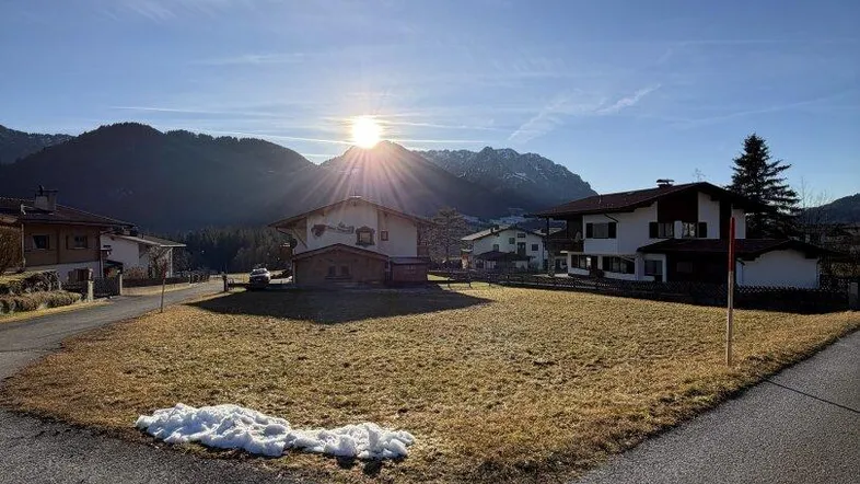 Sonniges Grundstück mit Bergblick und umliegenden Häusern in ländlicher Umgebung.