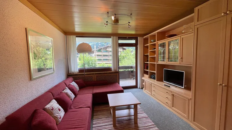 Wohnzimmer mit rotem Sofa, großem Fenster und Zugang zum Balkon mit Bergblick.