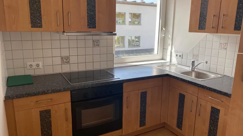 Funktionale Küche mit hellen Holzschränken, dunkler Arbeitsplatte, weißen Fliesen und Fenster.