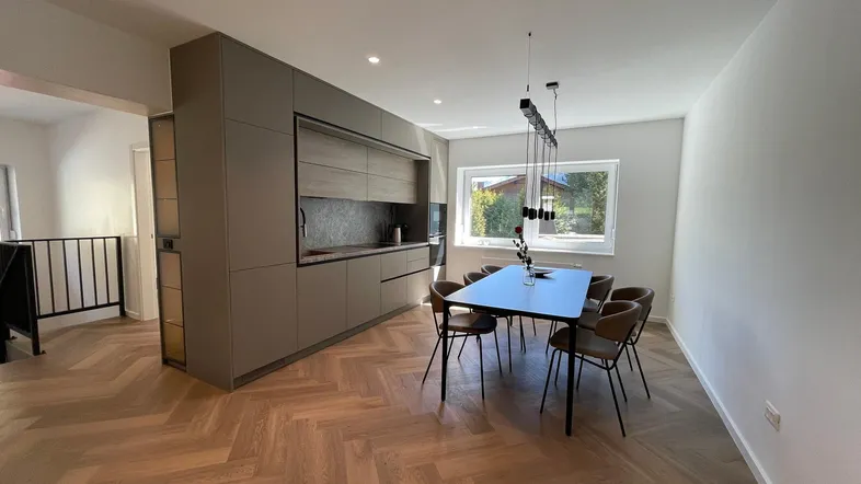 Moderne Einbauküche mit Essbereich, großem Esstisch und Fischgrätparkett.