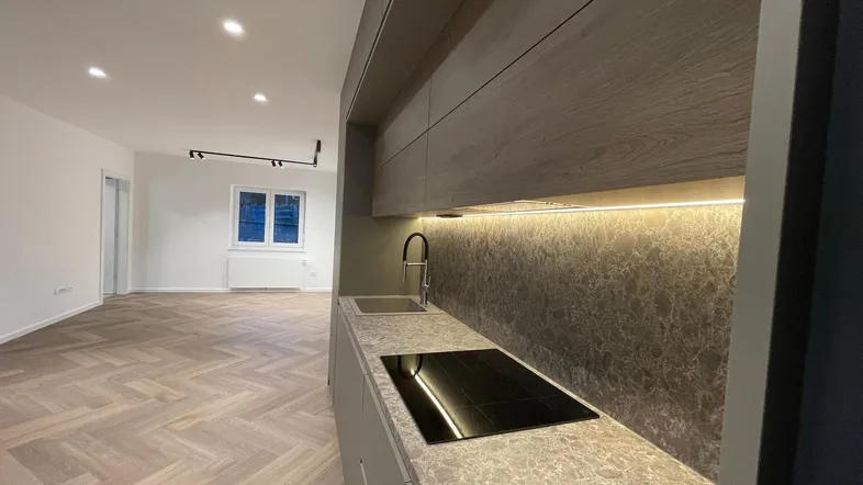 Moderne Küchenzeile mit Induktionskochfeld und Spüle, offen zum hellen Wohnbereich mit Fischgrätparkett.