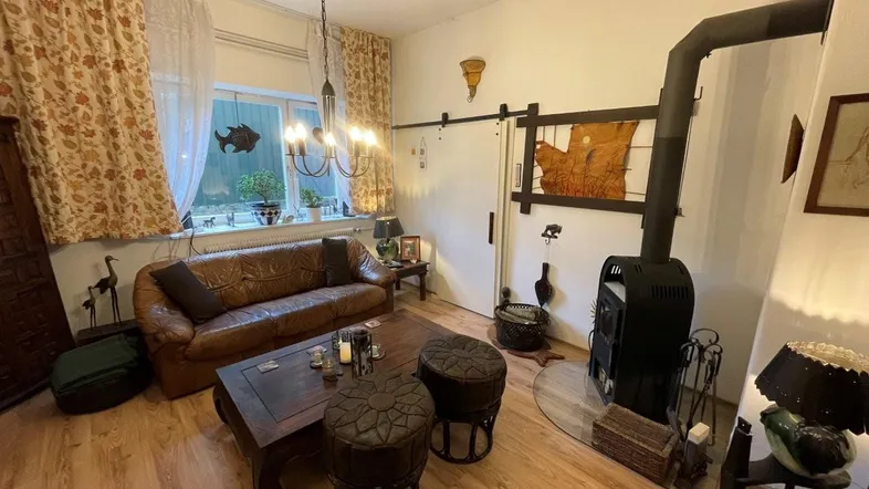 Gemütliches Wohnzimmer mit Kaminofen, Ledersofa und Holzboden, ideal für entspannte Abende.