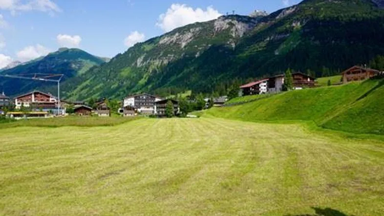 Grüne Wiesen und alpine Landschaft mit Häusern und majestätischen Bergen im Hintergrund an einem sonnigen Tag.