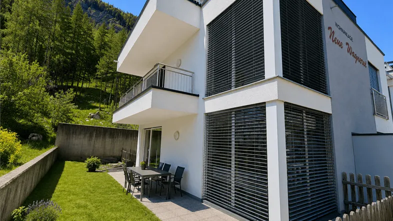Moderne Wohnanlage mit gepflegtem Rasen, Terrasse und Bergblick im Hintergrund.