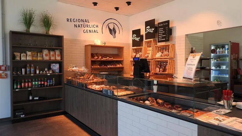 Helle Bäckerei mit Theke, Auslagen für Backwaren und Regalen mit regionalen Produkten.
