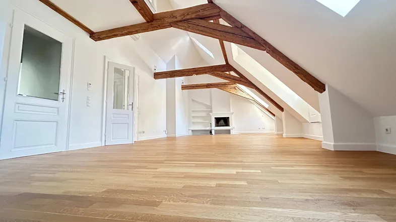 Geräumiges Wohnzimmer im Dachgeschoss mit Holzbalken, Parkettboden und Kamin.