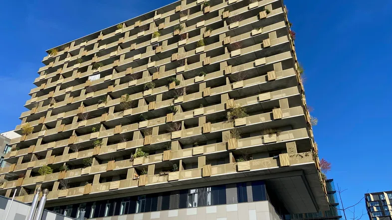 Modernes Wohngebäude mit zahlreichen Balkonen und begrünten Fassadenelementen unter blauem Himmel.