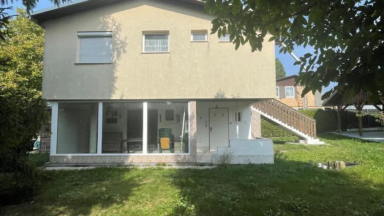 Einfamilienhaus mit heller Fassade, großen Fenstern im Erdgeschoss und weitläufigem Garten.