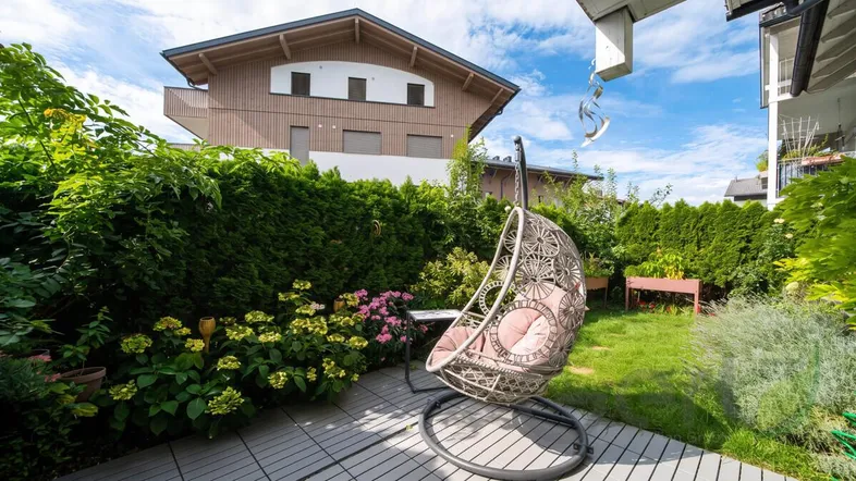 Gemütlicher Gartenbereich mit Schaukelstuhl und gepflegter Hecke vor einem Wohnhaus.