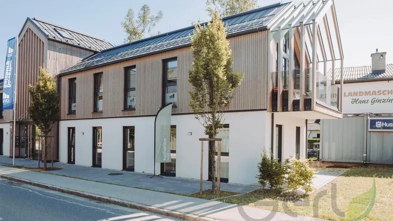 Modernes Gebäude mit Holz- und Weißfassade, großen Fenstern und einem markanten Giebelbereich an der Straße.