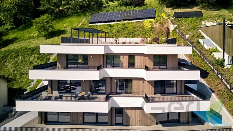 Modernes Mehrfamilienhaus mit großzügigen Balkonen, Dachterrasse und Photovoltaikanlage in grüner Hanglage.