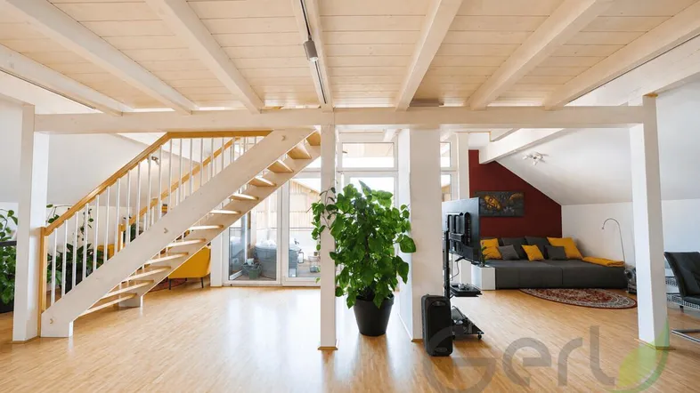 Heller, offener Wohnbereich mit sichtbaren Holzdeckenbalken und einer eleganten Holztreppe.