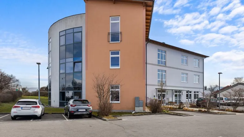 Modernes Geschäftsgebäude mit markanter runder Glasfassade und angrenzendem Parkplatz unter blauem Himmel.