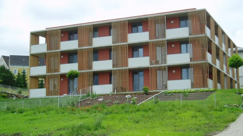 Modernes Mehrfamilienhaus mit Holzlamellenfassade und Balkonen auf einem begrünten Hang.