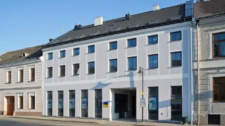 Mehrstöckiges Gebäude mit heller Fassade, vielen Fenstern und einem Durchgang im Erdgeschoss.