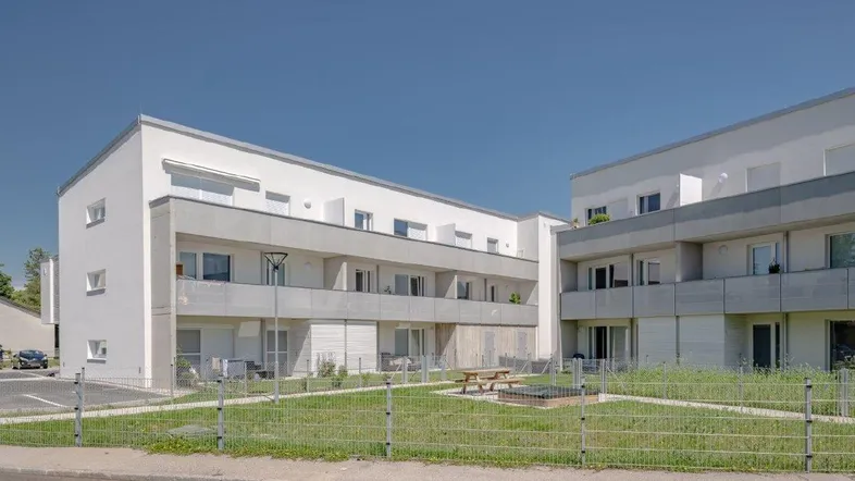 Moderne Wohngebäude mit Balkonen und einem gemeinschaftlichen Grünbereich mit Spielplatz.