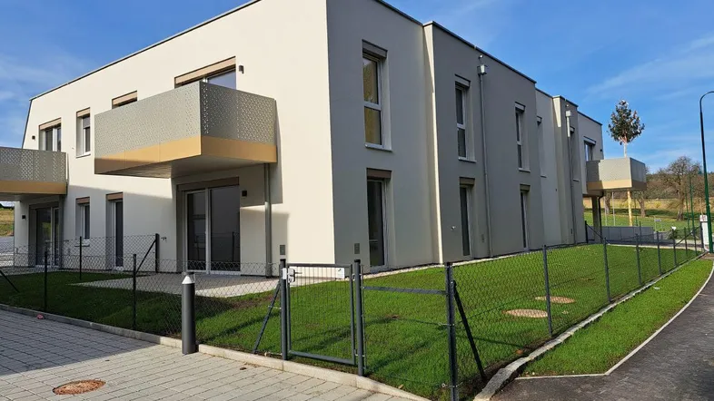 Modernes Mehrfamilienhaus mit heller Fassade, Balkonen und gepflegter Rasenfläche unter blauem Himmel.