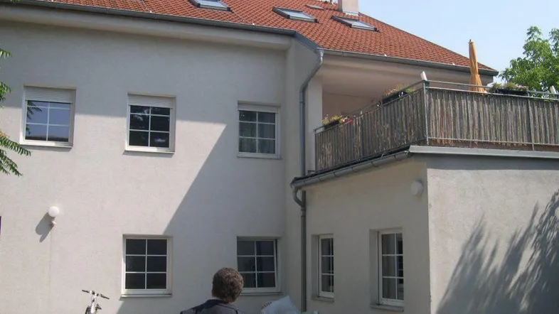 Ansicht der Gebäudefassade mit rotem Ziegeldach, Dachfenstern und einem möblierten Balkon.