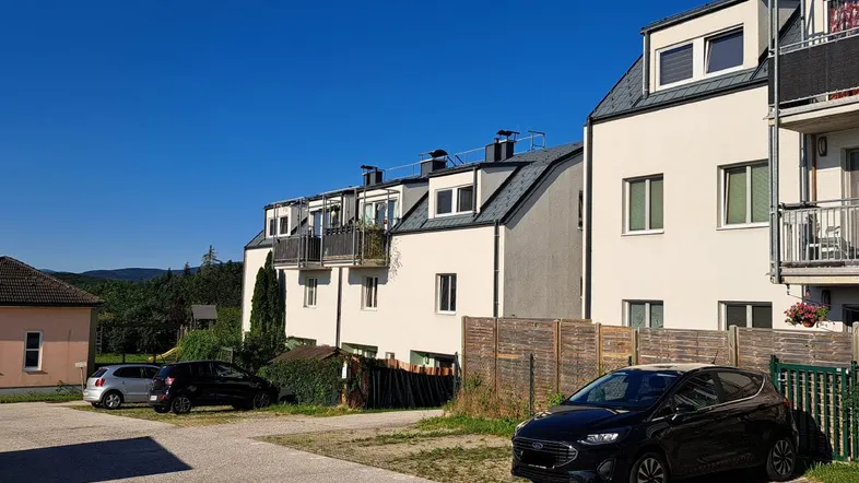 Mehrere moderne Wohngebäude mit weißer Fassade und Mansarddächern unter blauem Himmel.