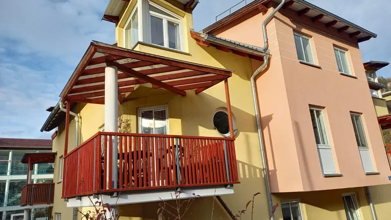 Modernes Mehrfamilienhaus mit farbiger Fassade und einem möblierten Balkon unter einem Vordach.