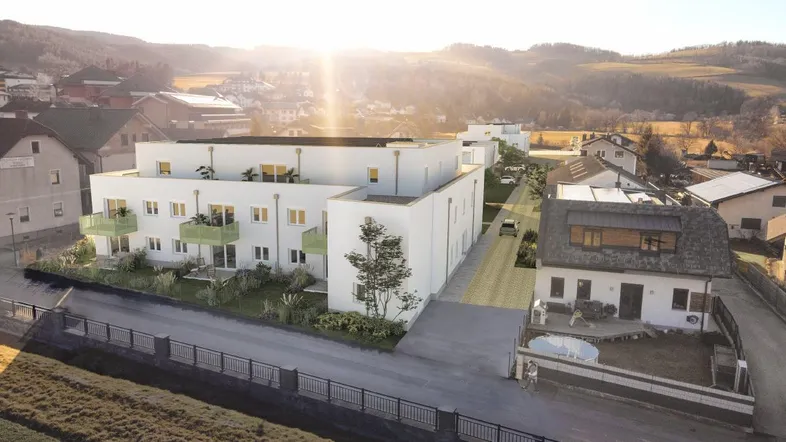 Luftaufnahme eines modernen Wohnkomplexes mit weißen Fassaden und grünen Balkonen in ländlicher Umgebung.