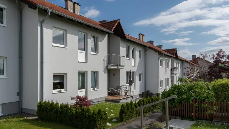 Außenansicht eines Reihenhauses mit kleiner Terrasse, Garten und gepflegter Hecke.