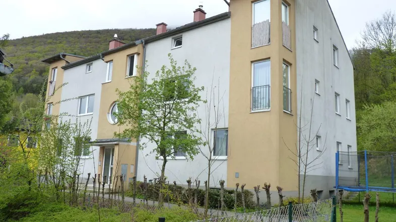 Mehrfamilienhaus mit heller Fassade, französischen Balkonen und umgebender Natur.