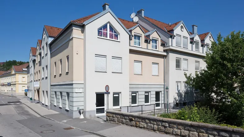 Mehrstöckiges Gebäude mit mehreren Giebeln und roten Ziegeldächern an einer ruhigen Straße.