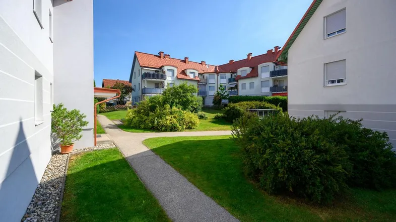 Grünanlage mit Gehwegen zwischen Wohngebäuden, umgeben von gepflegten Büschen und Bäumen.